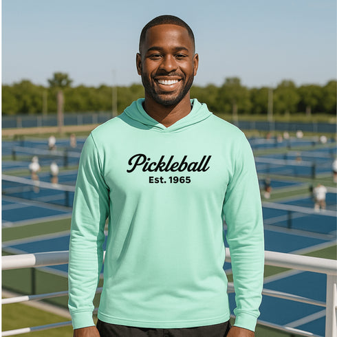 Man wearing a light blue hoodie with 'Pickleball Est. 1965' text on a pickleball court.